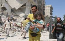 FILE: A Syrian man carries a child in a district of Aleppo after an air raid. Picture: AFP.