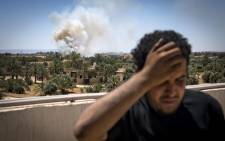 A fighter loyal to the internationally-recognised Government of National Accord (GNA) stands on a rooftop as smoke rises in the distance during clashes with forces loyal to strongman Khalifa Haftar, in Espiaa, about 40 kilometres south of the Libyan capital Tripoli on 29 April 2019. Picture: AFP