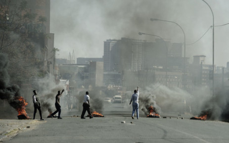 Protesters gesture towards police officers (not seen) as they burn tyres in Jeppestown, Johannesburg, on 11 July 2021. Picture: LUCA SOLA/AFP