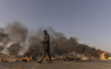 A man walks past a barricade in a road during a protest against illegal mining and rising crime in the area in Kagiso on 4 August 2022. Picture: GUILLEM SARTORIO/AFP