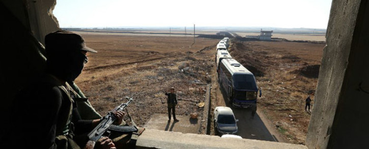 A member of Hayat Tahrir al-Sham group, led by Syria's former Al-Qaeda affiliate, watches as a convoy of buses gets ready to enter the towns of al-Foua and Kefraya to evacuate their residents on 18 July 2018. Picture: AFP.