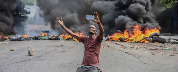 A man films himself in front of tyres on fire during a general strike launched by several professional associations and companies to denounce insecurity in Port-au-Prince on 18 October 2021. A nationwide general strike emptied the streets of Haiti's capital  on Monday, with organisers denouncing the rapidly disintegrating security situation highlighted by the kidnapping of American and Canadian missionaries at the weekend. Picture: Richard PIERRIN/AFP
