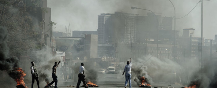 Protesters gesture towards police officers (not seen) as they burn tyres in Jeppestown, Johannesburg, on 11 July 2021. Picture: Luca Sola/AFP