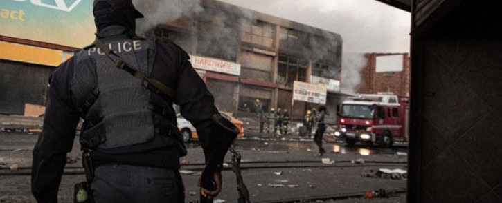 A police officer watches firefighters extinguish a building following riots in Alexandra on 12 July 2021. Picture: Boikhutso Ntsoko/Eyewitness News
