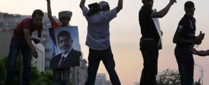 Supporters of deposed president Mohamed Morsi (on the poster) flash the sign of victory atop a wall during a rally outside the headquarters of the Republican Guard in Cairo on 9 July 2013. Egypt's armed forces warned in a statement against any attempt to disrupt the country's "difficult and complex" transition. Picutre:AFP