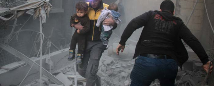 A Syrian man carries two children in the rubble of buildings following regime air strikes on the rebel-held besieged town of Douma in the eastern Ghouta region, on the outskirts of the capital Damascus, on 7 February 2018. Picture: AFP