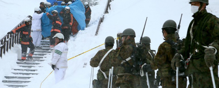 Firefighters carry a survivor rescued from the site of an avalanche in Nasu town, Tochigi prefecture, on 27 March, 2017, while Self Defense Force personnel look on. Picture: AFP.