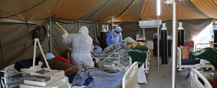 FILE: A professional healthcare worker wearing personal protective equipment (PPE) treats a patient in a tent dedicated to the treatment of possible COVID-19 coronavirus patients, while another cleans the ward at the Tshwane District Hospital in Pretoria on 10 July 2020. Picture: AFP