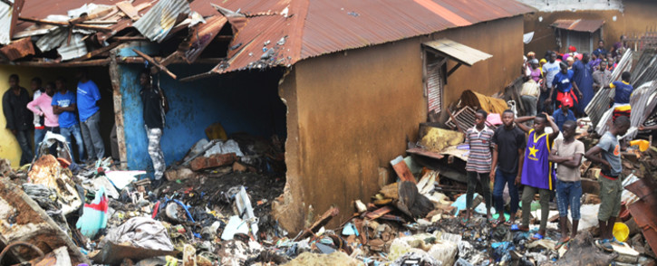 People stand near a damaged house after a rubbish dump collapsed the day before following heavy rain on the outskirts of Conakry. Picture: AFP.