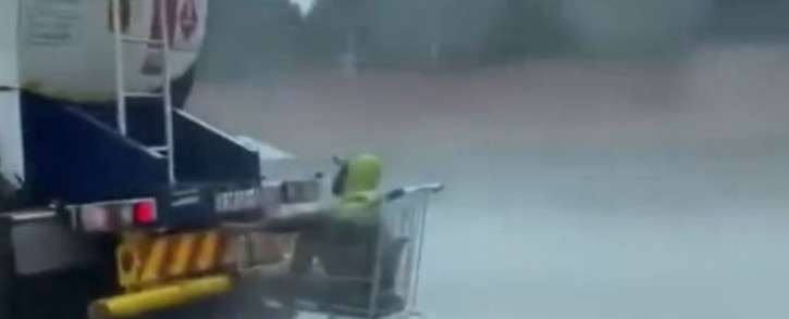 A screengrab of a man in a shopping trolley hitching a ride behind a fuel tanker in the rain outside Pretoria.