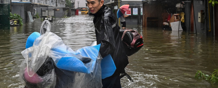 A man pushes a scooter while wading in a flooded street in a neighborhood in Ningbo, eastern China's Zhejiang province on 25 July 2021, as Typhoon In-Fa lashes the eastern coast of China. Picture: Hector RETAMAL / AFP