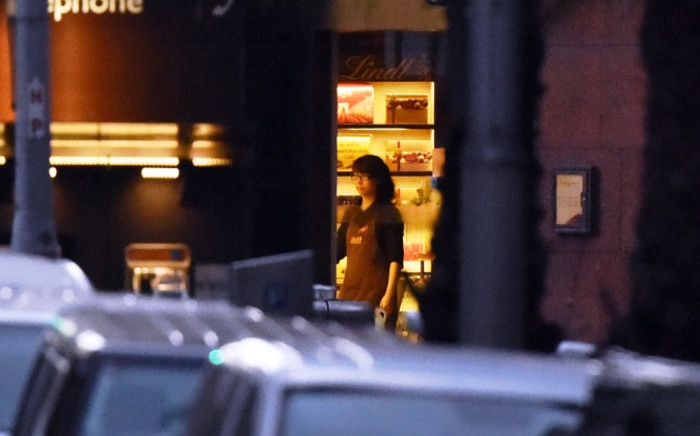 A female hostage stands by the front entrance of the cafe as she turns the lights off in the Sydney central business district on 15 December, 2014. Picture: AFP.