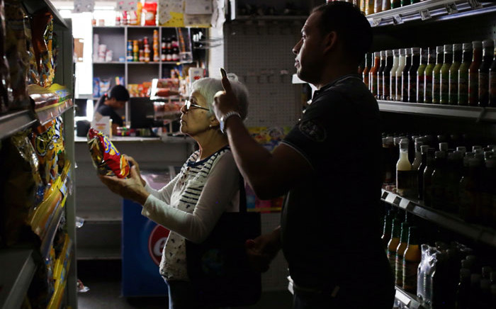 An employee uses his mobile phone torch to help a customer on 10 March 2019, during the third day of a massive power outage which has left Venezuelans without communications, electricity and water. Picture: AFP