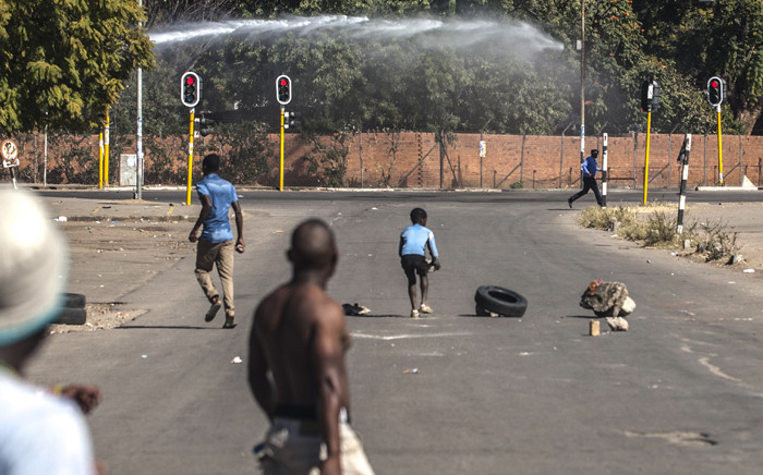 FILE: A man runs to cover from a police water cannon during during a demonstration on 6 July 2016 in Bulawayo in Zimbabwe. Picture: AFP.