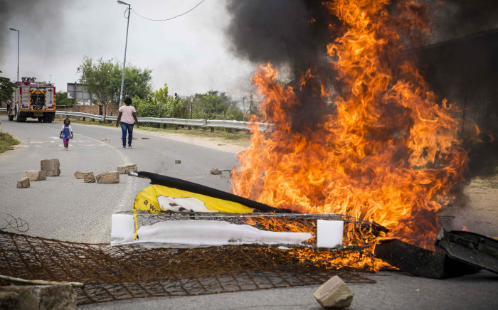 A woman and child walk past a burning barricade in Alexandra, put in place to close the road to the new clinic that was meant to be opened. Picture: Thomas Holder/EWN.