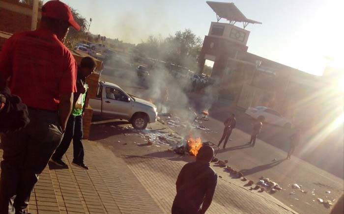 Residents walk pass stones and burning tyres outside North West Health Department head office in Mahikeng following a demonstration by staff after suspended HOD Thabo Lekalakala reported for duty. Picture: Supplied.