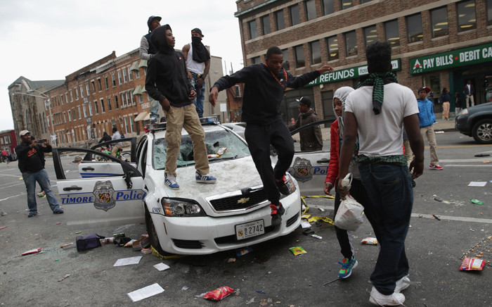 Demonstrators climb on a destroyed Baltimore Police car in the street near the corner of Pennsylvania and North avenues during violent protests following the funeral of Freddie Gray on 27 April, 2015 who died in police custody. Picture: AF