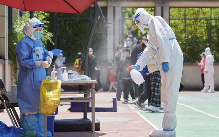 A community volunteer wearing personal protective equipment disinfects an area before conducting a test for the COVID-19 coronavirus in a compound during a COVID-19 lockdown in Pudong district in Shanghai on 17 April 2022. LIU JIN / AFP