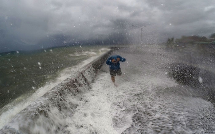 A resident walks past big waves spilling over a wall onto a coastal road in the city of Legaspi in Albay province, south of Manila on December 14, 2015, as typhoon Melor approaches the city. Picture: AFP /Charism Sayat.