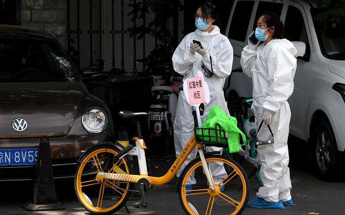 FILE: People wearing protective suits use their mobile phones near the Guang’an Sport Center where swab tests for people that live or visited Xinfadi market is taking place in Beijing on 15 June 2020. Picture: AFP