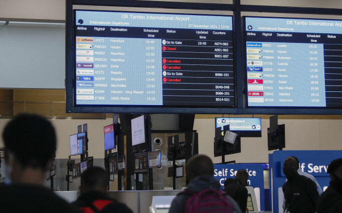 Travellers walk near an electronic flight notice board displaying cancelled flights at OR Tambo International Airport in Johannesburg on 27 November 2021. Picture: AFP