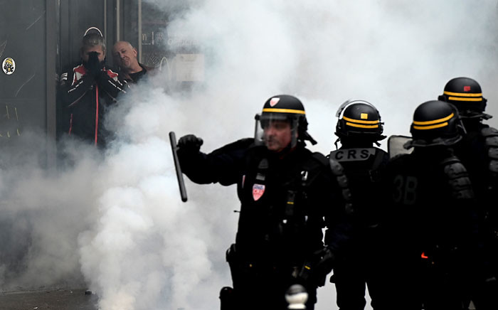 Protesters hide from tear gas smokes as riot police officers walk on place d'Italie in Paris on 16 November 2019. Picture: AFP