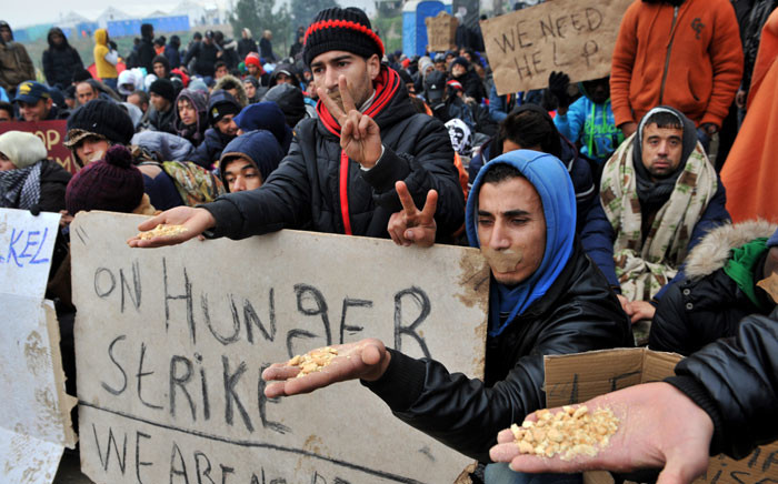 Migrants and refugees hold a placard (C) reading “on hunger strike” they wait to cross the border between Greece and Macedonia near the Greek village of Idomeni on November 21, 2015. Picture: AFP