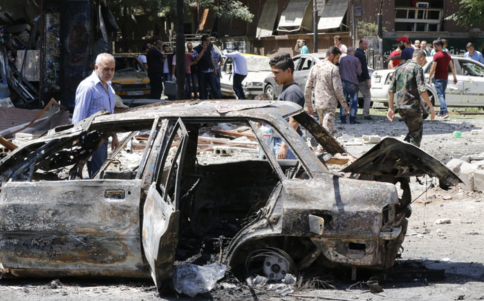FILE: Syrian men stand next to a charred vehicle as they inspect the damage at the site of a suicide bomb attack in the capital Damascus' eastern Tahrir Square district, on July 2, 2017. Picture: AFP.