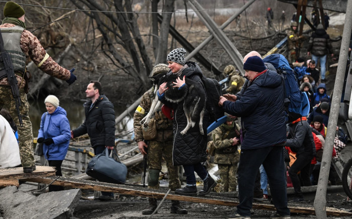A woman carries a dog while people cross a destroyed bridge as they evacuate the city of Irpin during heavy shelling and bombing on 5 March 2022. Picture: Aris Messinis/AFP