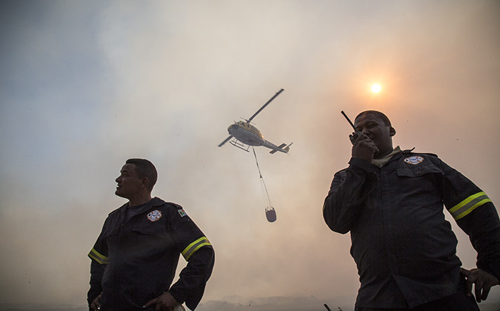 Two firefighters radio on the front lines of the fire while a helicopter prepares to water-bomb the raging flames. Picture: Thomas Holder/EWN