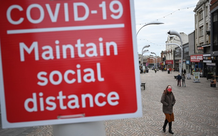 FILE: A woman wearing a face mask as a precaution against the transmission of the novel coronavirus walks by a sign encouraging social distancing in a street in Blackpool, Lancashire on 16 October 2020. Picture: AFP.