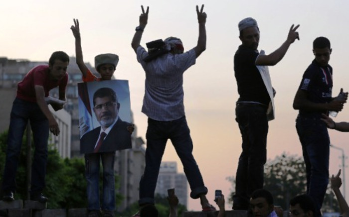 Supporters of deposed president Mohamed Morsi flash the sign of victory atop a wall during a rally outside the headquarters of the Republican Guard in Cairo on 9 July 2013. Picture: AFP
