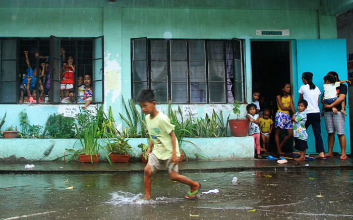 A young evacuee wades through flooded school grounds while others look on from a school building being used as an evacuation center in the city of Legaspi in Albay province, south of Manila on 14 December, 2015, as typhoon Melor approaches the city. Picture: AFP.