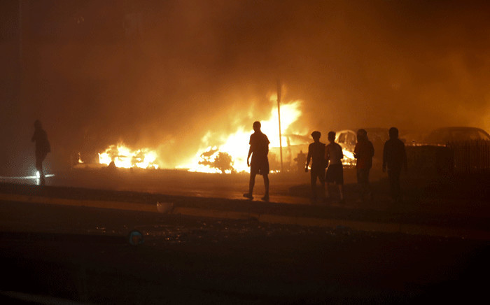 People walk by cars torched by protestors a few blocks from the County Court House during a demonstration against the shooting of Jacob Blake, who was shot in the back multiple times by police the day before, prompting community protests in Kenosha, Wisconsin on 24 August 2020. Picture: AFP