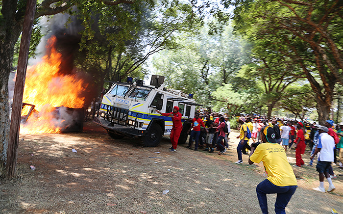 A group of students charge towards a police nyala blocking a blazing portable toilet during a student protest over proposed tuition fee hikes for the 2016 year at the Union Buildings in Pretoria on 23 October 2015. Picture: Reinart Toerien/EWN.