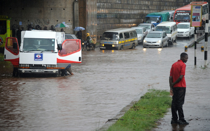 People try to push a truck across a flooded section of road, as a man stands on the side of the road on 29 April, 2016 in the Kenyan capital Nairobi that has been hit by heavy downpours as the long rains season starts. Picture: AFP.