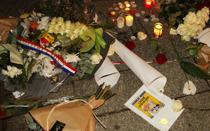 Flowers, candles and a picture of the front page of an edition of Charlie Hebdo are layed on the pavement near the offices of French satirical weekly Charlie Hebdo in Paris on 7 January, 2015, after armed gunmen stormed the offices leaving 12 dead. Picture: AFP.