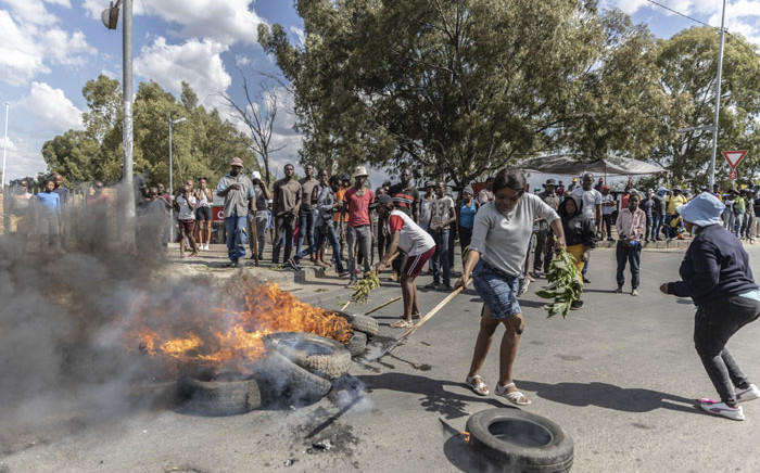 A woman positions a burning tyre as community members protest against the rise of crime in the area in Diepsloot, South Africa, on 6 April 2022. Picture: GUILLEM SARTORIO/AFP