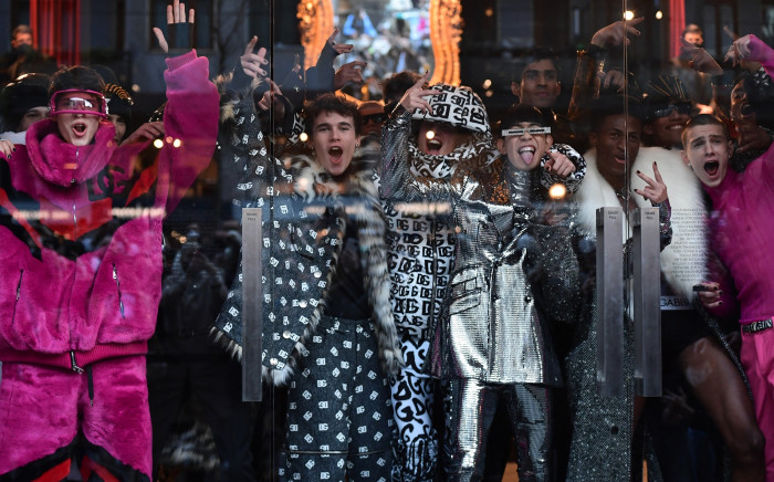 Models presenting creations for Dolce & Gabbana's Men's Fall/Winter 2022/2023 fashion collection gesture from behind a venue's glass door. Picture: AFP