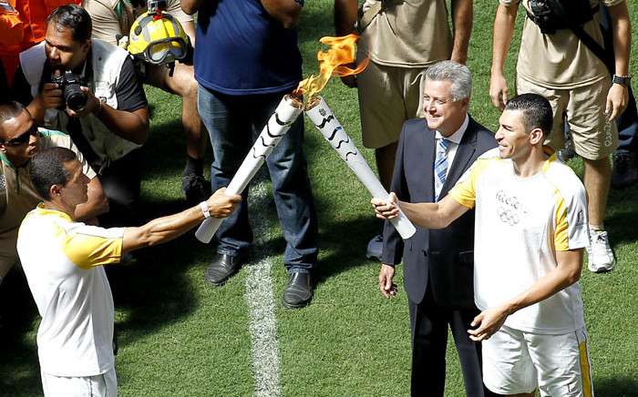 FILE: Brazilian former footballer Lucio (R) and Brasilia's governor Rodrigo Rollemberg receive the Olympic flame from fireman Haudson Alves at the field of the Brasilia National Stadium in Brasilia on 3 May 2016. Picture: AFP.