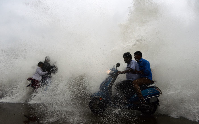 Indian residents ride a bike as waves hit a breakwater at Kasimedu fishing harbour as Cyclone Phethai approaches the eastern Indian coast, in Chennai on 16 December 2018. Picture: AFP