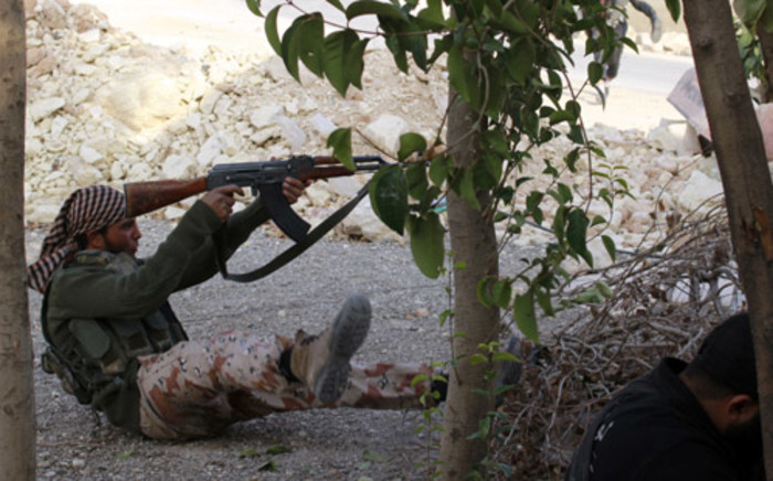 FILE: A Syrian rebel fighter shoots while sitting on the ground during clashes with pro-regime forces in Syria. Picture:AFP