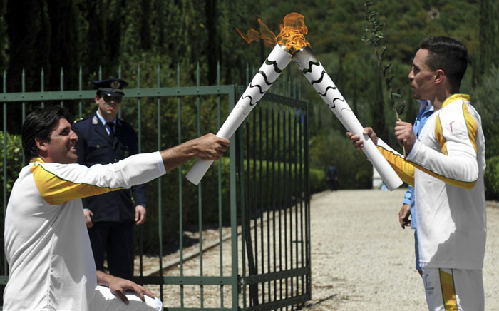 First torchbearer, world champion at the artistic gymnastics Lefteris Petrounias (R) passes the Olympic flame to second torchbearer, Brazilian volleyball player, Giovane Cavio during the torch relay, on 21 April 2016 in ancient Olympia. Picture: AFP