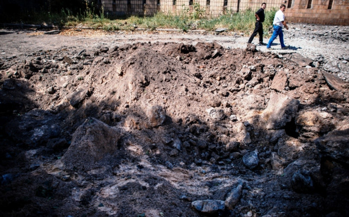 Men walk past a bomb hole in а street after an "air strike" overnight in Donetsk, on 6 August 2014. Picture: AFP.