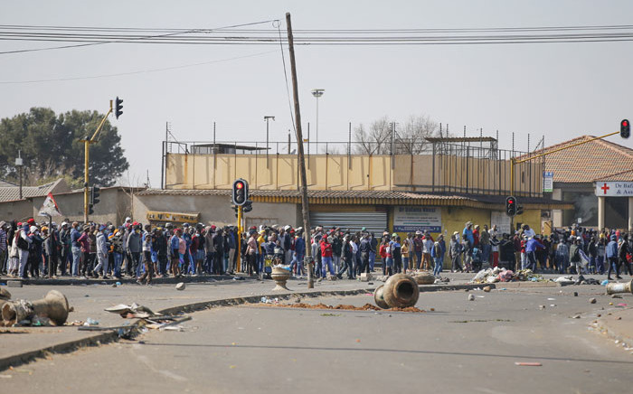 People stand near the looted and vandalised Lotsoho Mall in Katlehong township, east of Johannesburg, on 12 July 2021. Several shops are damaged and cars burnt in Johannesburg following a night of violence. Police are on the scene trying to control further protests. It is unclear if this is linked to sporadic protests following the incarceration of former president Jacob Zuma. Picture: Phill Magakoe/AFP