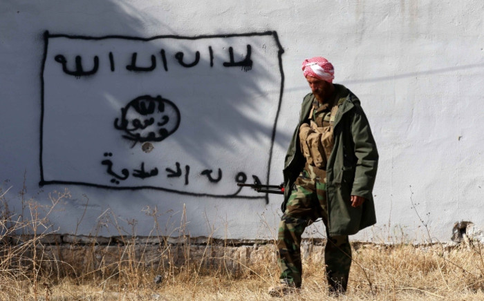 FILE: A Kurdish fighter walks by a wall bearing a drawing of the flag of the Islamic State (IS) group in the northern Iraqi town of Sinjar. Picture: AFP.