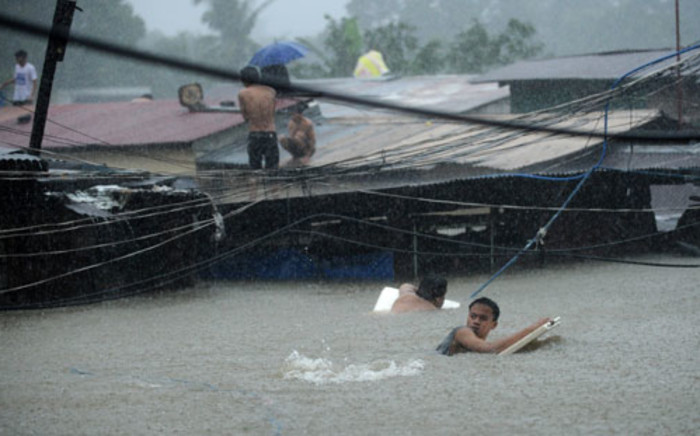 Residents try to cross through floodwaters as others wait on the roofs of their houses after a river overflowed in Manila on August 7, 2012, caused by torrential rains across the capital. Picture: AFP.