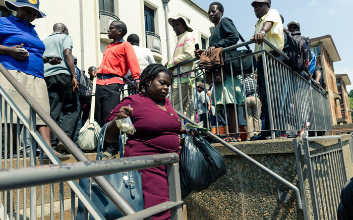 A woman with cash in hand walks past fellow bank customers queing to withdraw the new Zimbabwe currency in Harare on 12 November 2019. Picture: AFP
