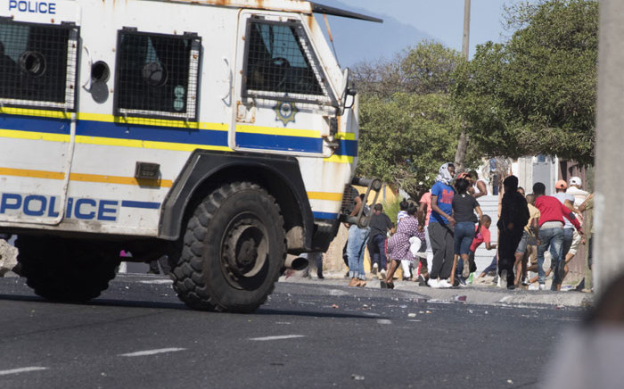 People run away as a South African Police Services armoured vehicle drives into a street during clashes with residents of Tafelsig, an impoverished suburb in Mitchells Plain, near Cape Town, on 14 April 2020, after some people in the community did not receive food parcels which were being handed out as part of the support for this community during the nationwide lockdown to curb the spread of the COVID-19 coronavirus. Picture: AFP