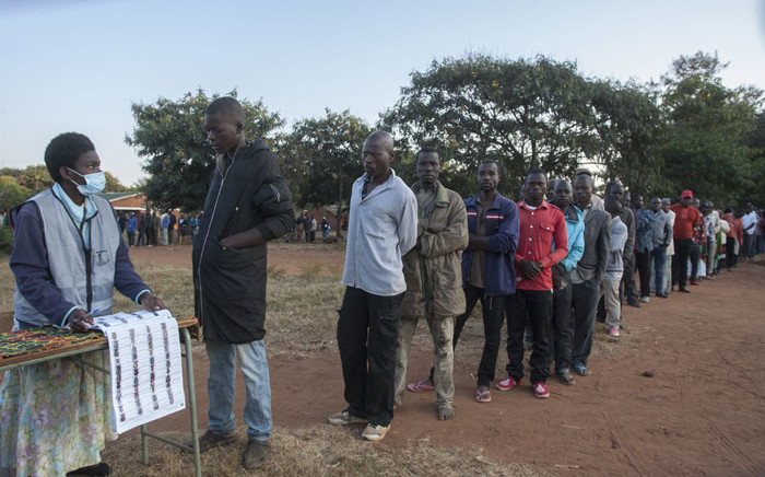 An electoral official (L) checks the voters' roll while people queue to vote at the Malembo polling station during the presidential elections in Lilongwe on 23 June 2020. Picture: AFP